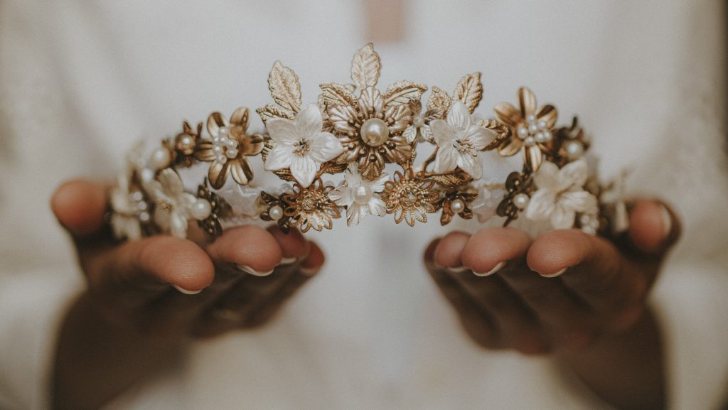 Diadema artesanal dorada con flores blancas y perlas, sostenida entre las manos.